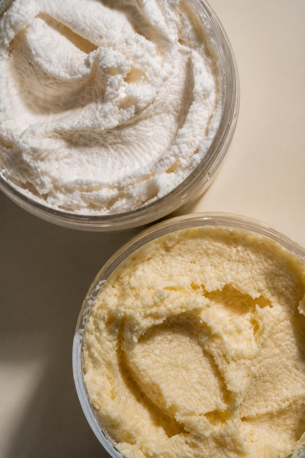 Two open jars of freshly whipped body butter, one ivory and one golden