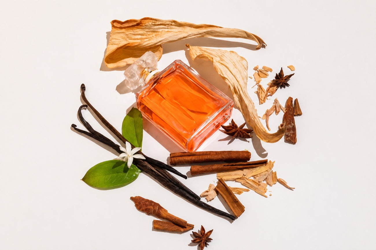A glass bottle surrounded by vanilla pods, cinnamon, star anise and dried botanicals