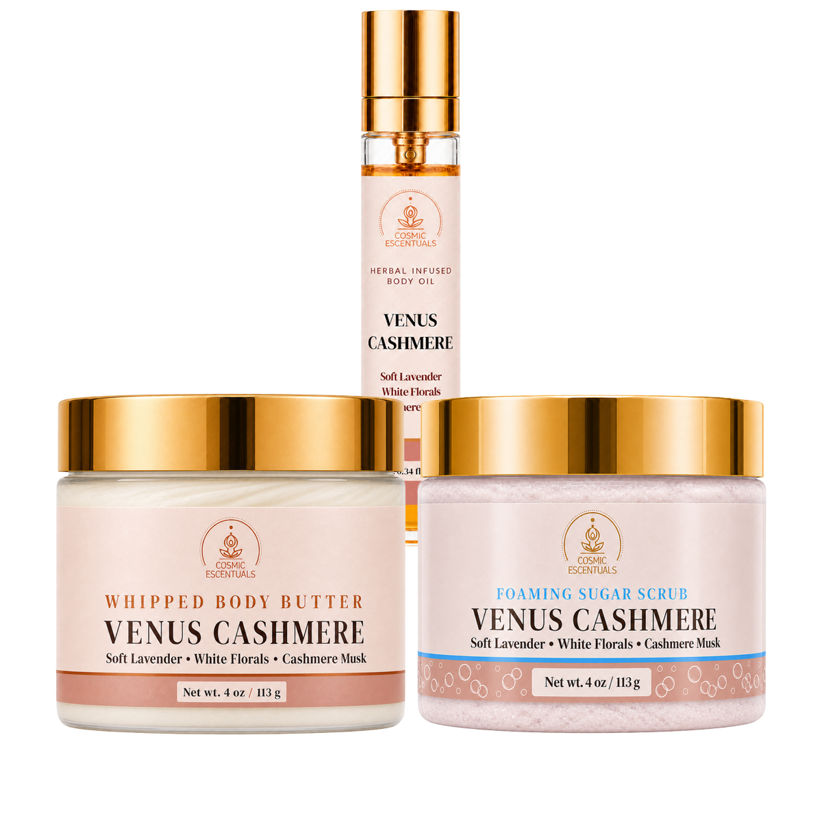 Three Venus Cashmere skincare products from Cosmic Escentuals on a white background: a whipped body butter jar, a foaming sugar scrub jar, and a body oil spray bottle, all with gold caps and pale pink labels.
