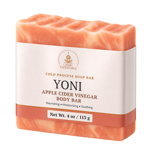 A single bar of Cosmic Escentuals Yoni Apple Cider Vinegar Body Bar soap, shown in a peachy-orange color with a white paper label band around the middle, on a solid white background.