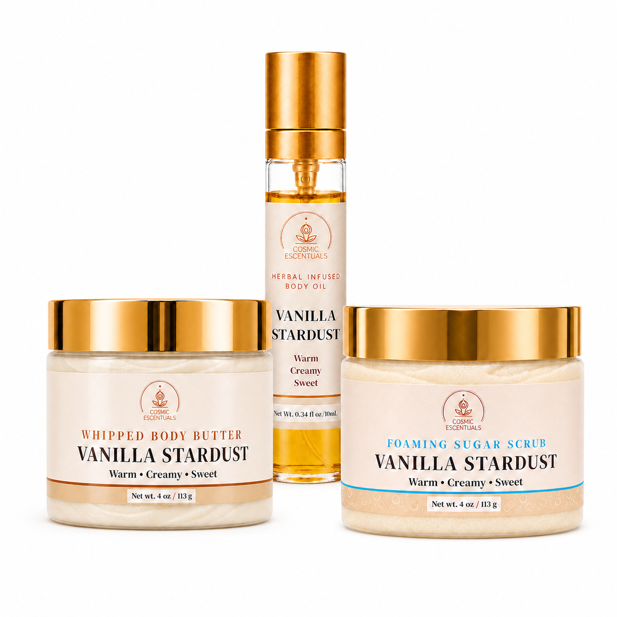 Three skincare products from Cosmic Escentuals arranged on a white background: a whipped body butter jar, a foaming sugar scrub jar, and a body oil bottle. The products have gold lids, cream-colored labels, and are filled with light beige products.