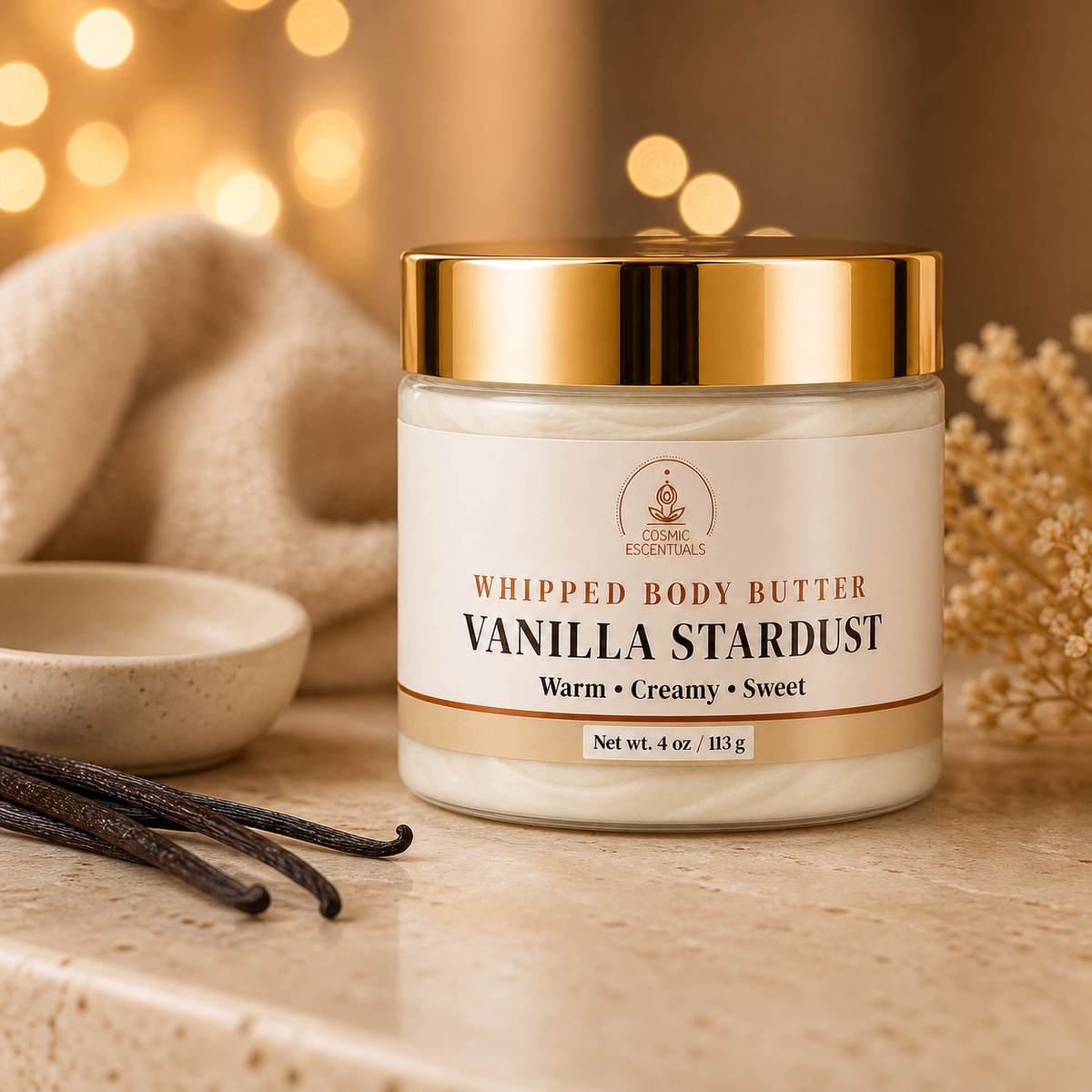 A jar of Vanilla Stardust Whipped Body Butter by Cosmic Escentuals sits on a stone surface with vanilla beans, a small bowl, and warm bokeh lights in the background.