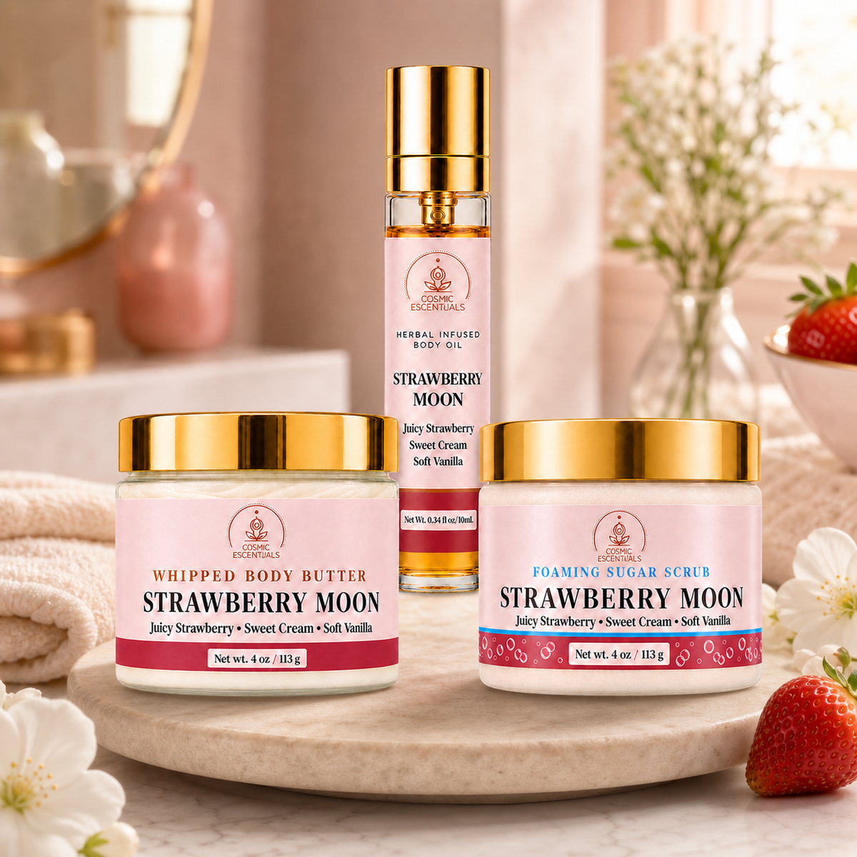 Three Cosmic Escentuals Strawberry Moon products arranged on a marble tray with strawberries and white flowers in a soft, warm-toned bathroom setting: a whipped body butter jar, a foaming sugar scrub jar, and a spray bottle of herbal infused body oil.