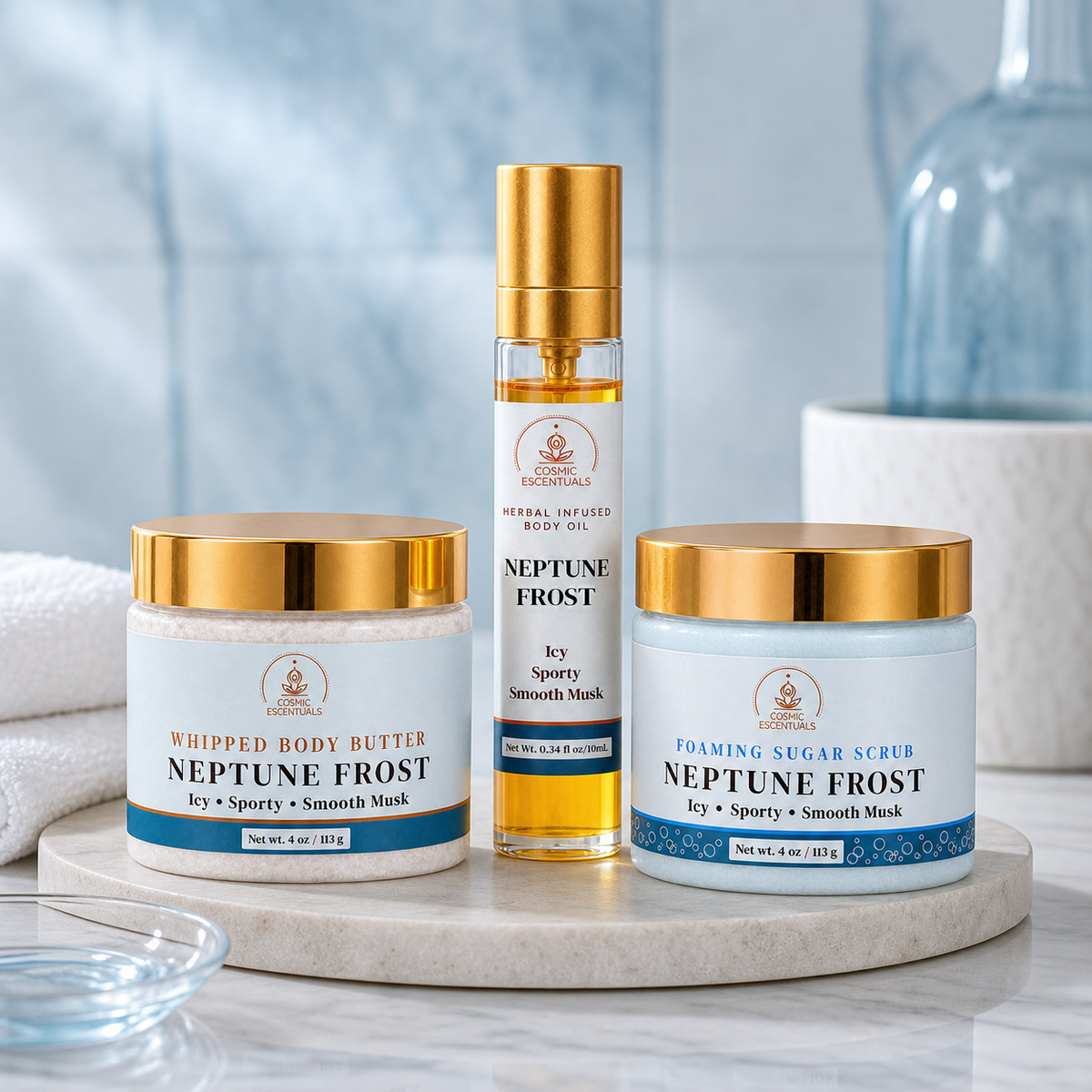 Three skincare products from Cosmic Escentuals on a white marble tray: a whipped body butter jar labeled Neptune Frost, a clear bottle of infused body oil with a gold cap labeled Neptune Frost, and a foam sugar scrub jar labeled Neptune Frost. The products are styled against a soft, blurred blue background with a glass bottle and towel.