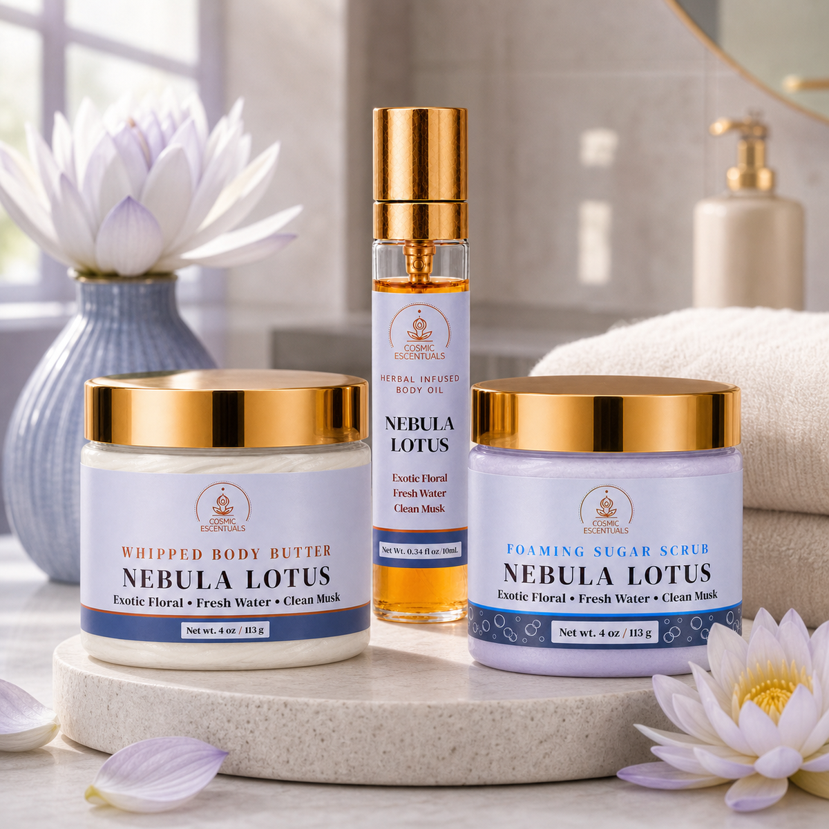 Three skincare products from Cosmic Escentuals arranged on a stone tray in a bright bathroom setting: a whipped body butter jar, a body oil bottle, and a foaming sugar scrub jar, all labeled Nebula Lotus with gold lids.