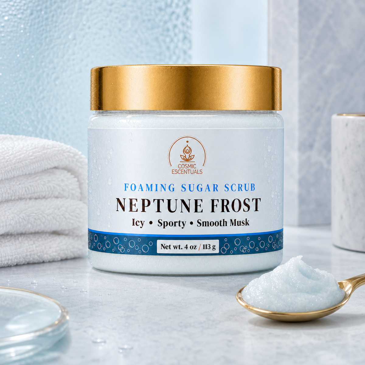 A jar of Cosmic Escentuals Neptune Frost Foaming Sugar Scrub, featuring a white jar with a metallic gold lid and a blue-and-white label, set on a marble surface with a gold spoon of white scrub and a folded towel in the background.