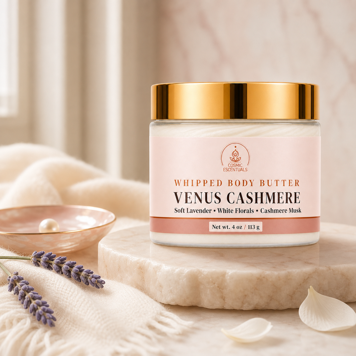 A jar of Venus Cashmere Whipped Body Butter by Luxe Essentials, styled on a marble slab with lavender sprigs, a small dish, and soft cream fabric in a warm, soft-focus setting.