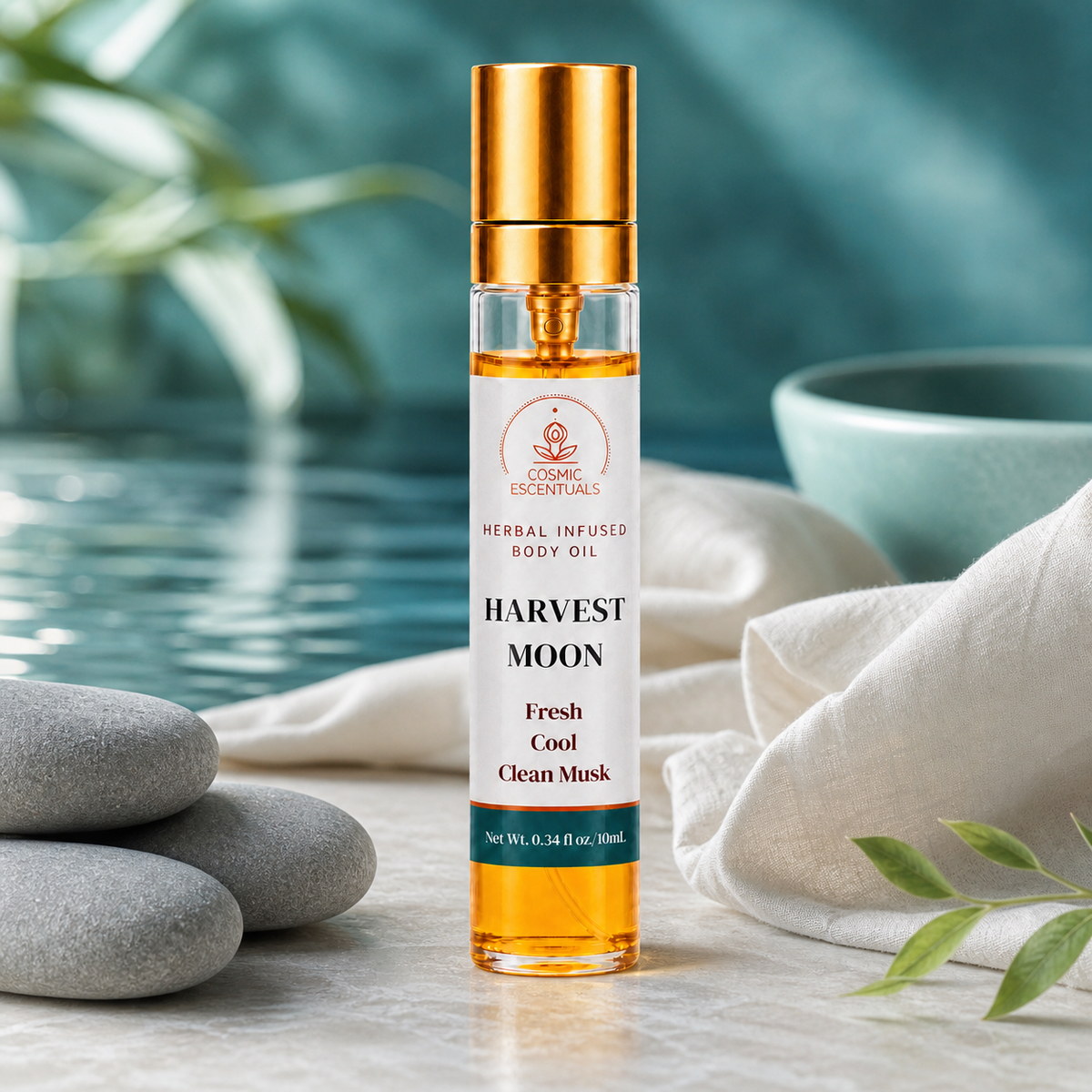 Harvest Moon Herbal Body Oil Spray on a pale stone ledge with stacked grey pebbles, a white linen cloth and a green sprig, still water behind.