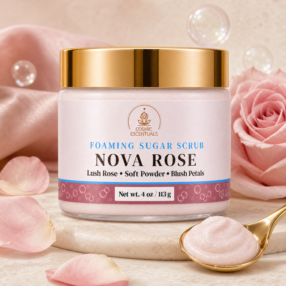 A jar of Nova Rose Foaming Sugar Scrub by Cosmic Escentuals, featuring a gold lid and a white label with blue and pink accents, styled with pink rose petals, a pink rose, and a gold spoon on a marble slab.