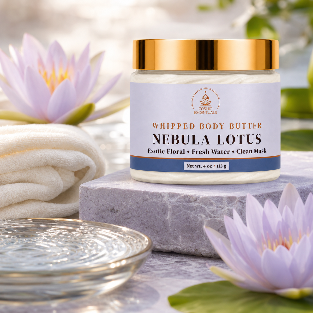 A jar of Whipped Body Butter labeled 'Nebula Lotus' by Luxe Essentials, styled on a gray stone slab with a white towel, a glass dish, and purple lotus flowers in a bright, soft-focus setting.