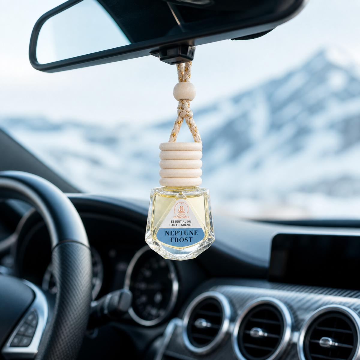 A car air freshener bottle labeled 'Neptune Frost' hanging from a rearview mirror inside a car, with snowy mountains visible through the windshield.
