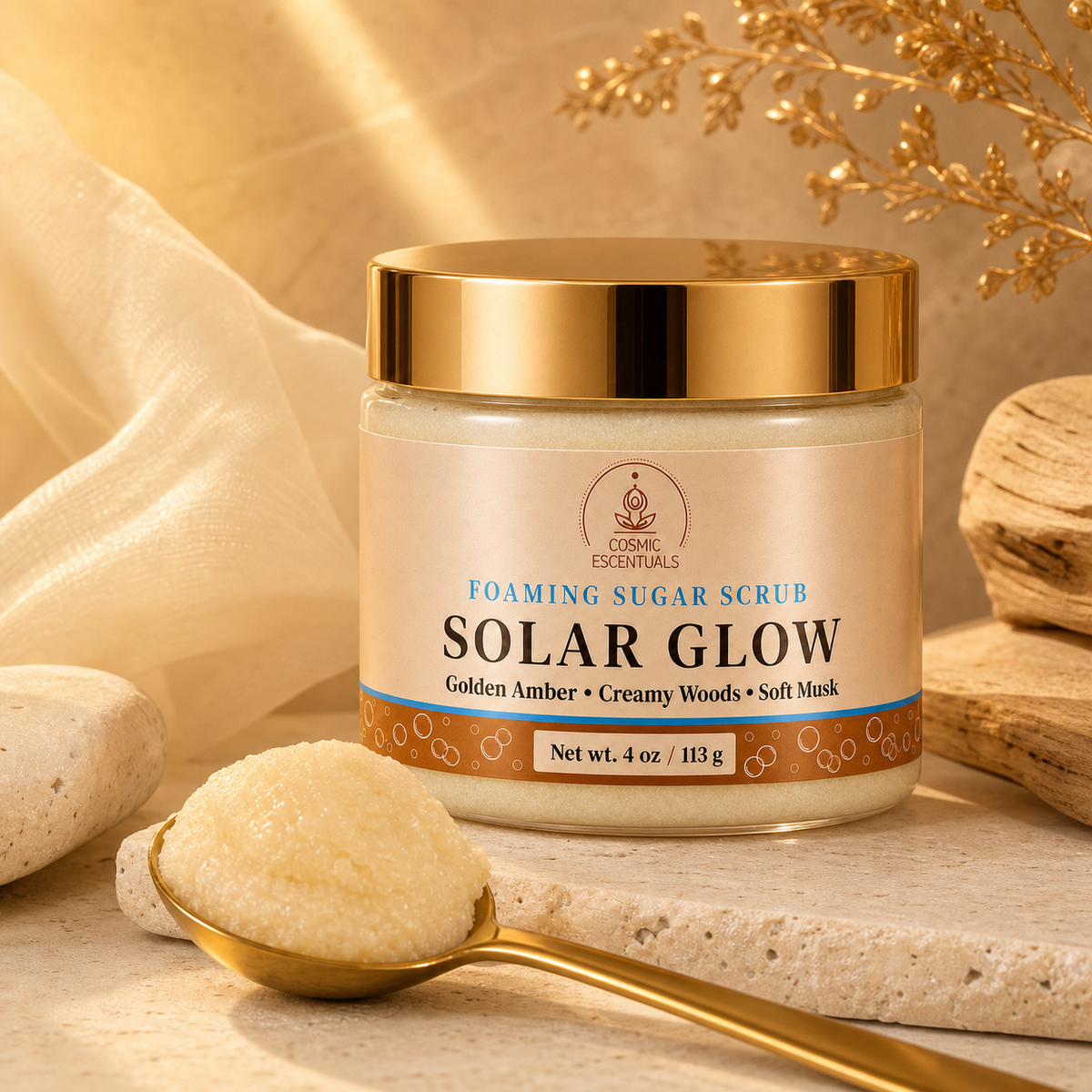 A jar of Cosmic Escentuals Solar Glow Foaming Sugar Scrub, styled on a stone surface with a gold spoon holding some of the scrub and decorative natural props in the background.