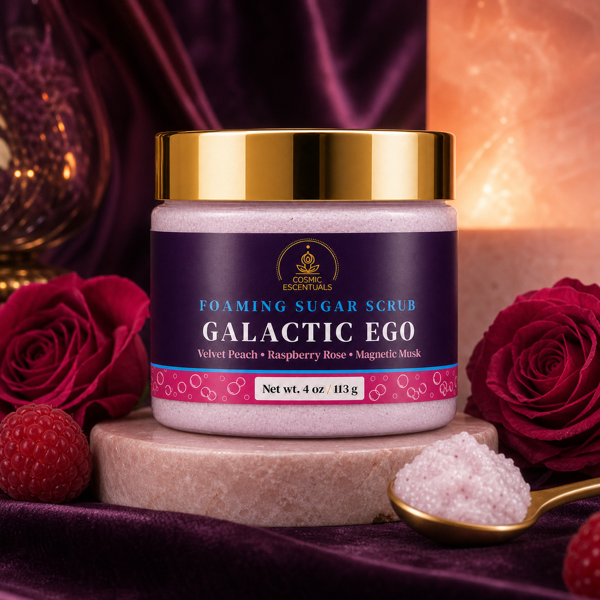 A jar of Cosmic Escentuals Galactic Ego Foaming Sugar Scrub, set on a stone pedestal with red roses, raspberries, and a gold spoon against a dark purple and warm orange background.