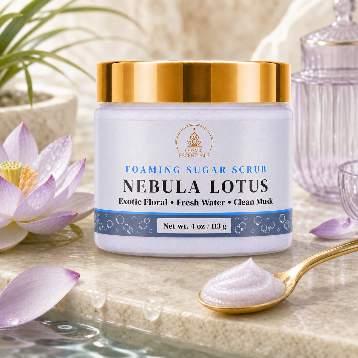 A jar of Cosmic Essentials Nebula Lotus Foaming Sugar Scrub sits on a marble surface surrounded by lotus flowers, petals, and a gold spoon with scrub, in a clean, styled setting.