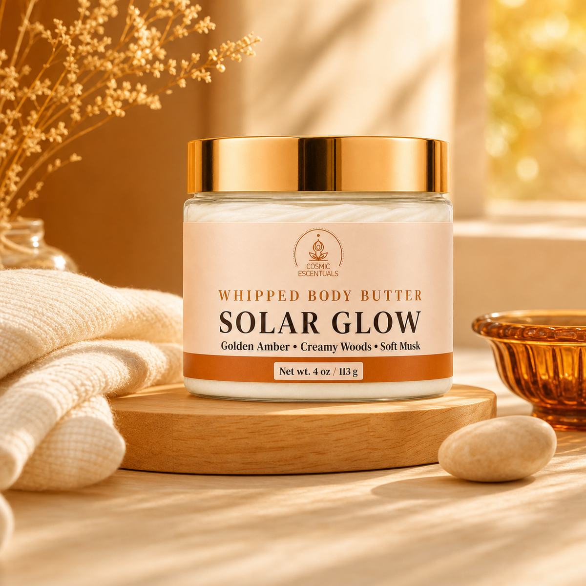 A jar of Cosmic Escentuals Solar Glow whipped body butter sits on a wooden tray on a warm, sunlit tabletop with a folded cream towel, dried flowers, and a small amber bowl nearby.