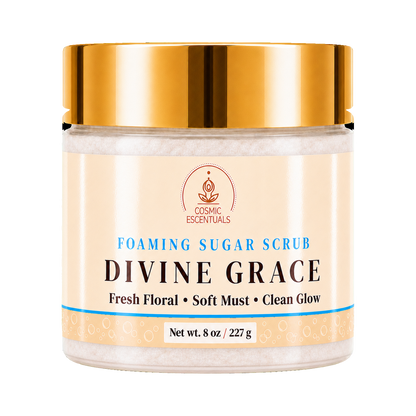 A jar of Divine Grace Foaming Sugar Scrub by Cosmic Essentials, featuring a shiny gold lid and a cream-colored label with blue and black text, set against a plain white background.