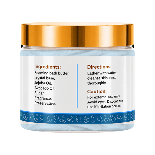 A jar of foaming bath butter with a metallic gold lid and a white label displaying ingredients, directions, and caution details. The jar is filled with light blue bath butter crystals and features a blue patterned band near the bottom.