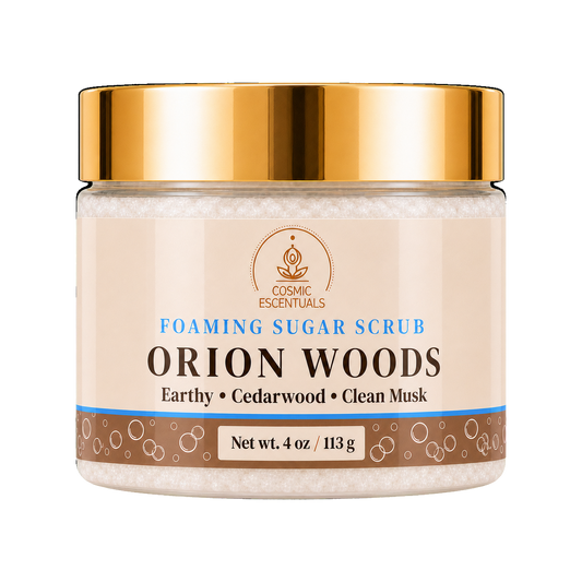 Cosmic Escentuals Orion Woods Foaming Sugar Scrub, 4oz jar with a shiny gold lid and a beige label, on a plain white background.