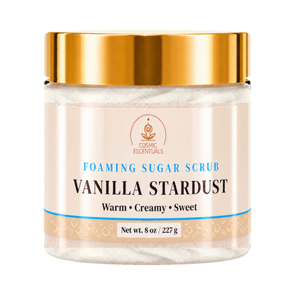 A jar of Cosmic Essentials Vanilla Stardust Foaming Sugar Scrub, featuring a metallic gold lid and a cream-colored label with blue and black text, set against a plain white background.
